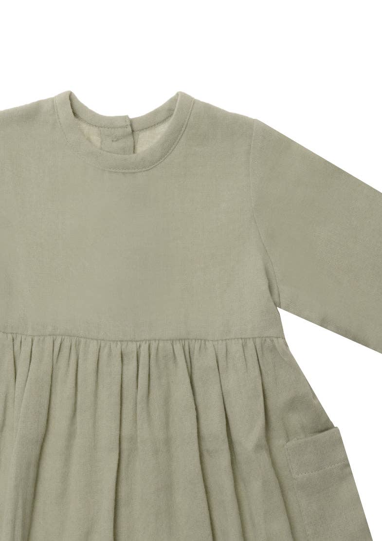 Baby Kleid aus Musselin in schilf mit langen Ärmeln, aufgesetzten Taschen und Knöpfen am Rücken, bequem und atmungsaktiv aus Baumwolle.